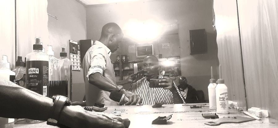 A barber trimming a client's beard by a window, photographed in warm light.