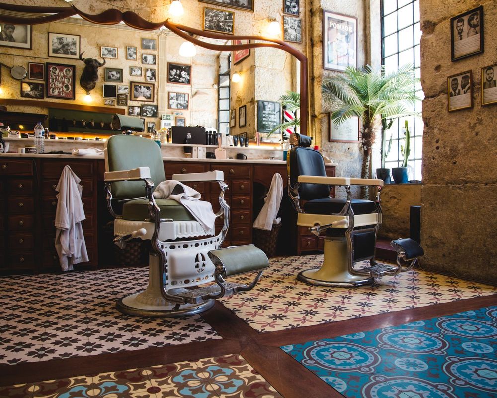 Inside the shop: two cast iron barber chairs, a checked tile floor and framed photographs on the wall.