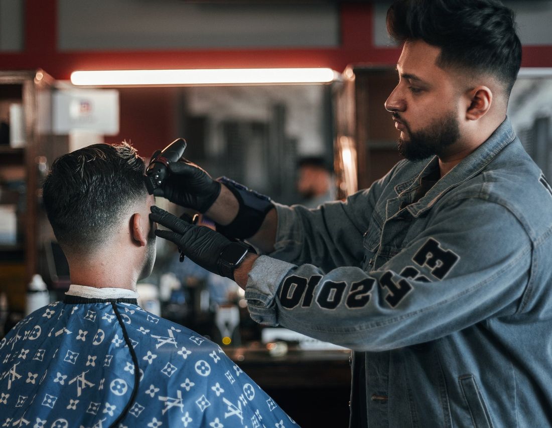 A barber in a denim jacket taking a fade down to the skin