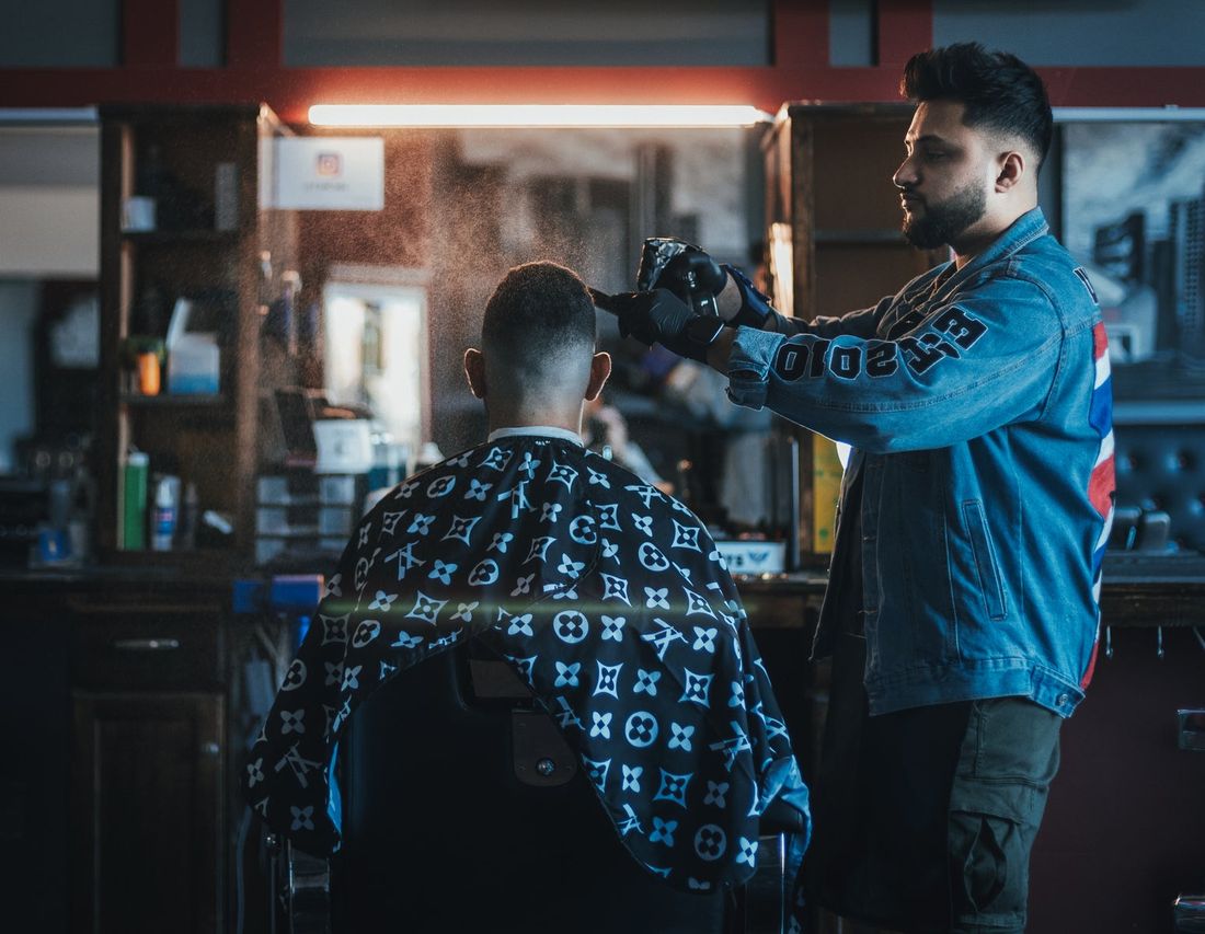 A barber wetting a client&rsquo;s hair down with a spray bottle before cutting