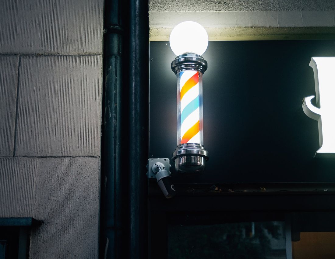 The barber pole outside the shop, lit up in the evening