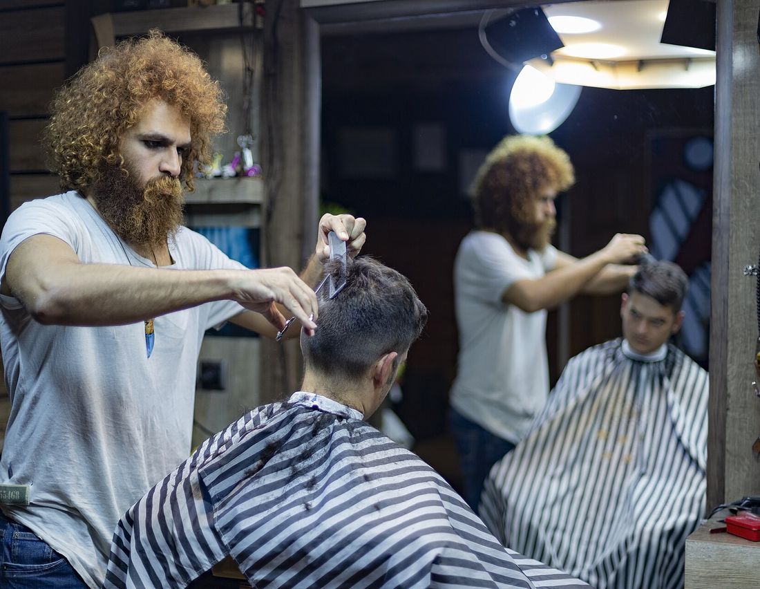 A barber finishing a client&rsquo;s cut, seen in the mirror