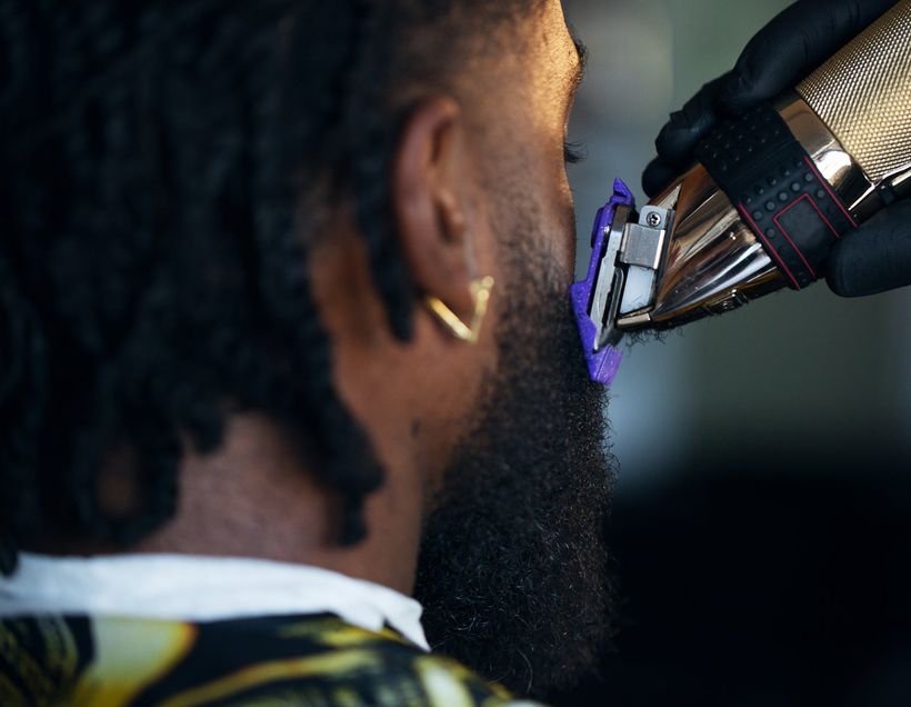 A barber shaping a client's beard along the jawline with a trimmer.