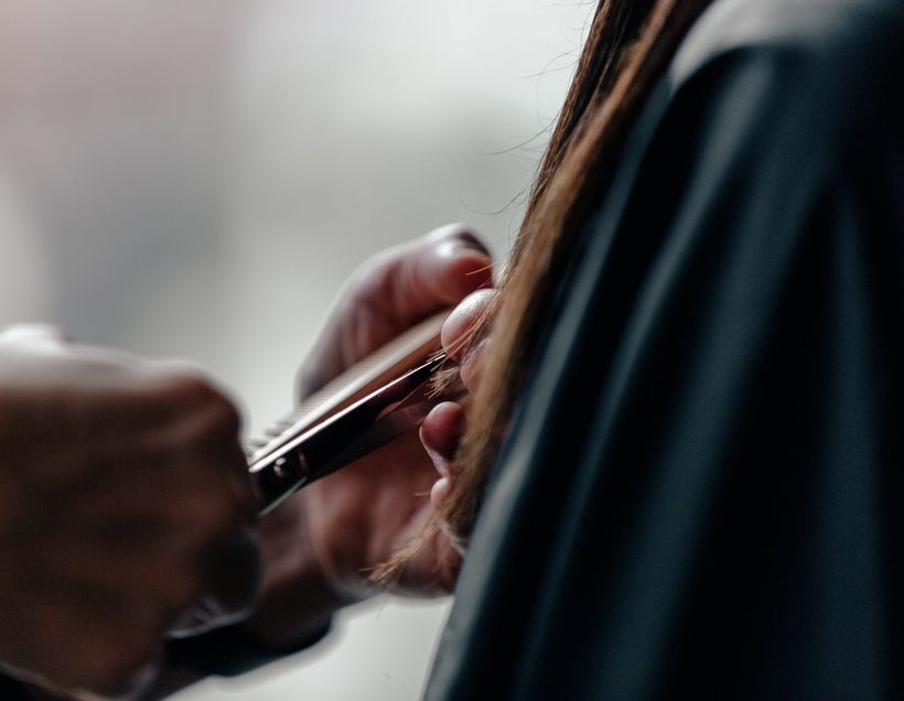 Scissors held mid-cut, a section of hair lifted between comb and fingers.